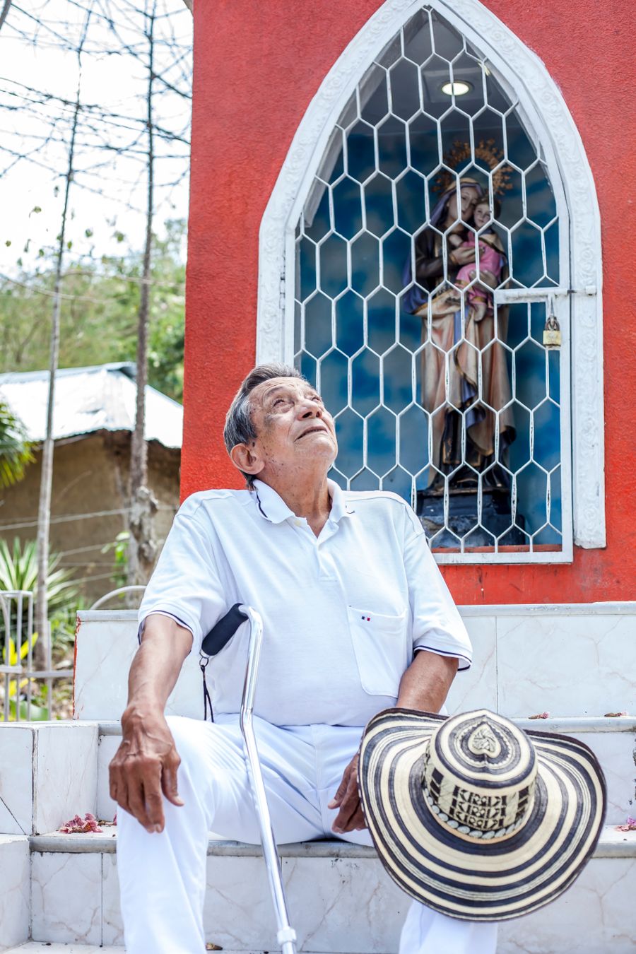 Señor mayor sosteniendo un sombrero vueltiao junto a una capilla en Colombia